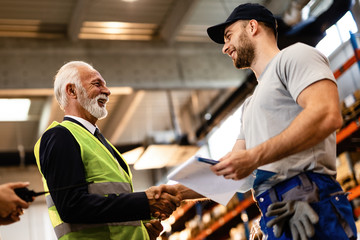 Wall Mural - Below view of happy mature manager shaking hands with a worker in industrial building.