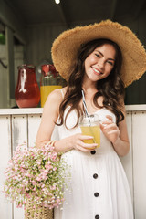 Poster - Cheerful happy young pretty woman outoors in park posing in hat holding juice.