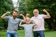 © Iryna - Portrait og happy family - grandpa, father and his son smiling and showing their muscles outdoor in park on background. Three different generation concept.