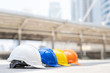 © methaphum - orange, yellow, blue and white hard safety wear helmet hat in the project at construction site building on concrete floor on city. helmet for workman as engineer or worker. concept safety first