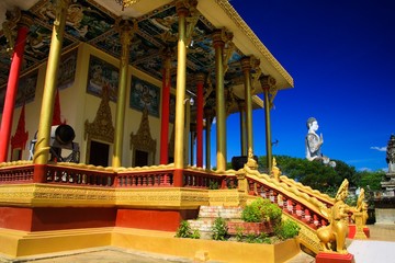 Wall Mural - View on golden pillars, drum and white buddha statue against blue sky at Buddhist temple - Wat Ek Phnom, near Battambang, Cambodia