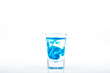 Blue food coloring diffuse in water inside shot glass with empty copyspace area for slogan or advertising text message, over isolated white background.