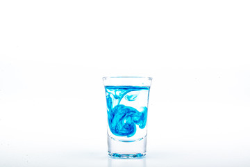 Blue food coloring diffuse in water inside shot glass with empty copyspace area for slogan or advertising text message, over isolated white background.