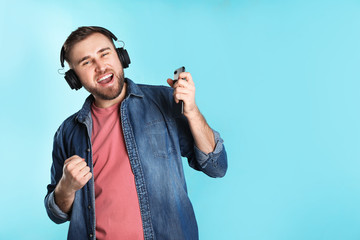 Wall Mural - Handsome man with mobile phone enjoying music in headphones on color background. Space for text