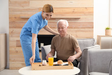 Nurse serving breakfast to elderly man indoors. Assisting senior people
