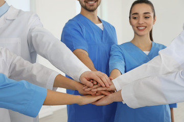 Wall Mural - Team of medical workers holding hands together indoors. Unity concept