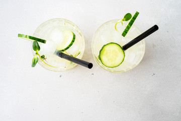 Top view of two glasses with Fresh Summer Healthy homemade mojito lemonade or cocktail with cucumber garnished with slice lime and micro greens on light background.