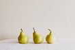 Closeup of three pears on white tablecloth against neutral wall background