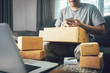 © wutzkoh - Asian young man using smart phone for checking shipment at home.