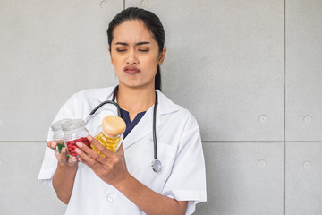 A Asian woman doctor holding bottles of medicine in her hands looking unhappy and upset.