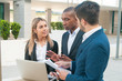 © Mangostar - Focused business colleagues arguing while collaborating on project. Men and woman in office suits standing outdoors with laptop and papers and talking, male coworker gesturing. Cooperation concept