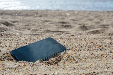 mobile phone lying on the beach in the sand. weatherproof phones, lost phone concept, data loss.