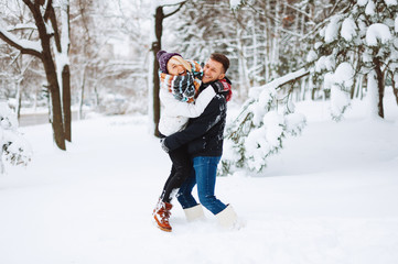 Young happy couple are playing in snow and enjoying their time together in park in winter.