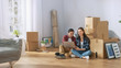 © Gorodenkoff - Happy Young Couple Sitting on the Floor of the Newly Rented / Purchased Apartment Use Laptop Computer. Unpacked Cardboard Boxes and Covered Furniture in the Modern Bright Sweet Home.