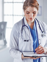 Wall Mural - Young woman doctor is standing with board with clipboard smilin