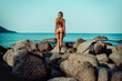Back view:  Slim Girl  in a bikini standing on rocks looking at blue  ocean. Phuket. Thailand.