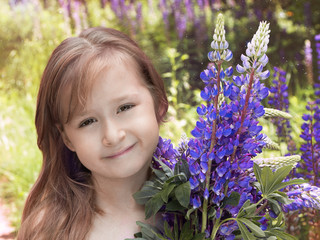 Portrait of a little pretty girl with flowers of lupins. Summer holidays, school holidays.