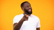 © motortion - Young black man pointing finger on camera and smiling against yellow background