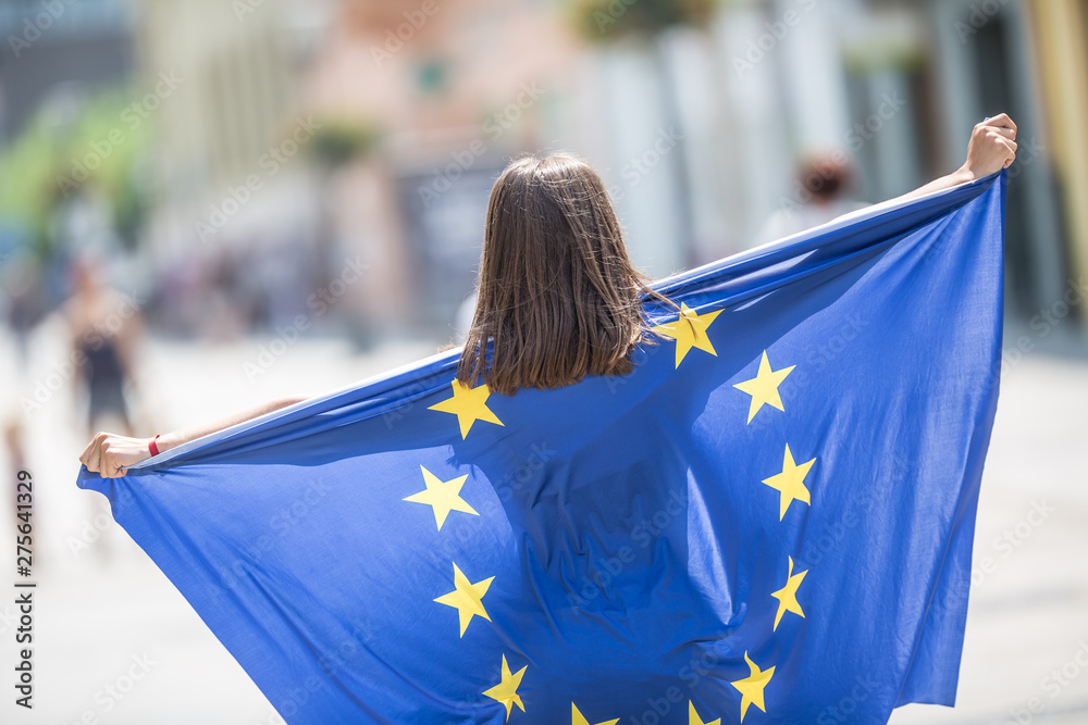 Cute happy young girl with the flag of the European Union in the streets somewhere in europe - obrazy, fototapety, plakaty 