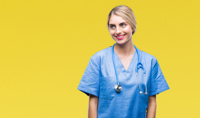 Poster - Young beautiful blonde doctor surgeon nurse woman over isolated background looking away to side with smile on face, natural expression. Laughing confident.