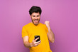 © luismolinero - Handsome over isolated purple wall with phone in victory position