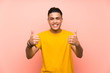 © luismolinero - Young man with yellow shirt over isolated pink wall giving a thumbs up gesture