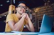 © BullRun - Portrait of cheerful male it professional working remotely with modern laptop device sitting at table and smiling at camera during break, happy man programmer in eyewear for vision correction