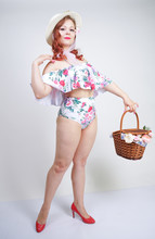 Beautiful Young Pin Up Caucasian Girl In Romantic Fashionable Straw Hat, Vintage Swimsuit With Flowers And Retro Wicker Basket Posing On White Background In Studio Alone. Pretty Pinup Woman Relaxing.