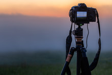 Black Digital Camera On Tripod Shooting Foggy Morning Landscape At Summer With Selective Focus