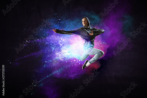 Modern female dancer jumping in hoodie with colourful splashes background. Mi...