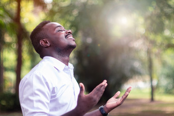 african man praying for thank god with light flare in the green nature