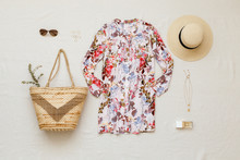Floral Shirt Dress, Straw Boater Hat, Wicker Beach Bag, Sunglasses, Gold Necklace And Perfume On Beige Background. Overhead View Of Woman's Summer Or Beach Outfit. Flat Lay, Top View.