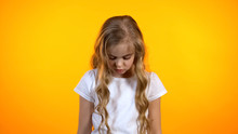 Blond Curly Girl Looking Down Isolated On Orange Background, Feeling Guilty