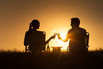 Young happy couple sitting together at sunset enjoying a glass of wine 