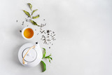 Tea concept with white tea set of cups and teapot surrounded with fresh tea leaves on concrete background with copy space.