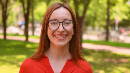 Poster - Charming Smiling Red Haired Woman Standing Middle Green Park. Wearing Red Shirt And Glasses. Natural Beauty Concept.