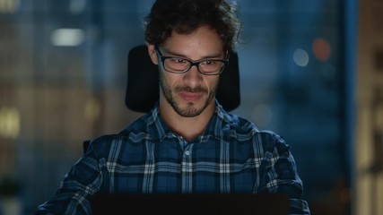 Wall Mural - Portrait of the Handsome and Successful Young Creative Entrepreneur Working at His Desk Using Laptop Computer. Working from Cozy Home Office / Studio at Night. 