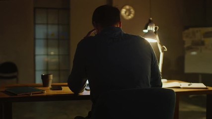 Wall Mural - Professional Creative Man Sitting at His Desk in Office Studio Working on a Laptop in the Evening. Man working with Data and Analyzing Statistics. 360 Degree Tracking Arc Shot Movement