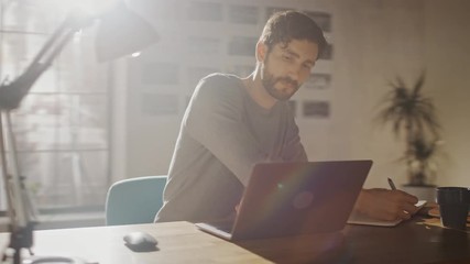 Poster - Professional Creative Man Sitting at His Desk in Home Office Studio Working on a Laptop Drinks Beverage from the Cup. Energetic Fast Paced Movement. Camera Moving Around. 360 Degree Tracking Arc Shot