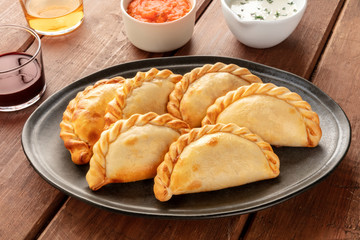 Wall Mural - A closeup of Argentinian empanadas with sauces and wine on a dark rustic wooden background