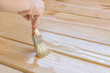 Applying varnish paint on a wooden surface. Man hand with a brush closeup. Painting wood wall and  floor.