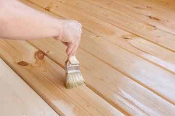 Applying varnish paint on a wooden surface. Man hand with a brush closeup. Painting wood wall and  floor.