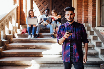 Wall Mural - Portrait of smiling african american student looking at cellphone, behind sitting his friends.