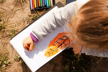 Little girl draws a tree with colored pencils