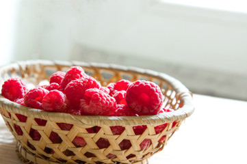 Wall Mural - raspberries in a basket on a light wooden background