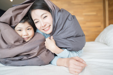 Wall Mural - Mother and her daughter child girl playing in the bedroom and putting blanket on . Happy Asian family