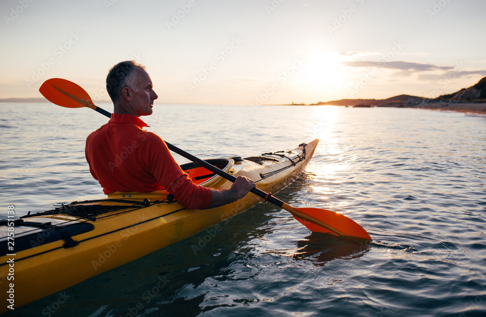 Senior man paddling kayak on the sunset sea - obrazy, fototapety, plakaty 
