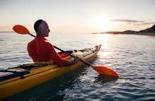 Senior Man Paddling Kayak On The Sunset Sea