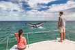 © Maridav - Whale watching boat tour tourists people on ship looking at humpback tail breaching ocean in tropical destination, summer travel vacation. Couple on deck of catamaran.