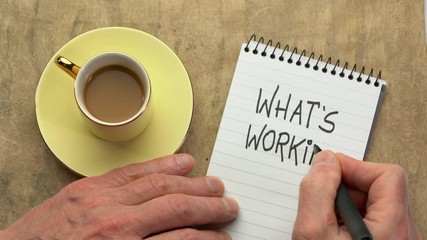 Wall Mural - What's working?  A man hand writing a note with a black marker in a spiral notebook, overhead view